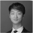 Black and white portrait of an Asian man in a suit and tie smiling slightly against a plain background.
