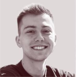 Young man with short hair smiling against a plain light background.
